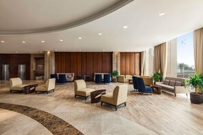 A spacious lobby with multiple seating areas, a reception desk, and a large window providing a view. - Levatio Hotel (Muscat)