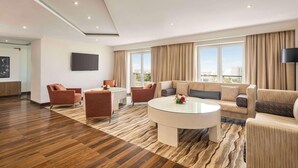 A modern hotel room with a wooden floor, a round glass coffee table, a sofa, and a TV mounted on the wall. - Levatio Hotel (Muscat)