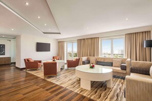 Una habitació d'hotel moderna amb un terra de fusta, una taula de cafè rodona de vidre, un sofà i un televisor penjat a la paret.