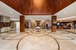 Una hall d'albergo con reception, area salotto e un elemento decorativo centrale.