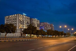 A multi-story hotel with a modern facade, illuminated signage, and a well-lit street in the foreground. - Levatio Hotel (Muscat)