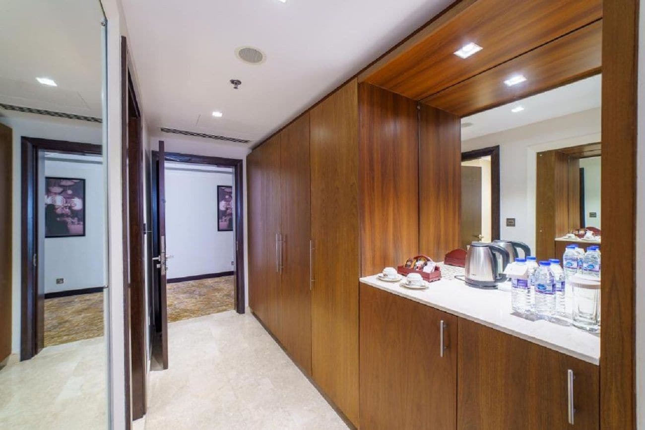 Habitación de hotel con un armario de madera, un espejo, una encimera con una tetera, tazas y agua embotellada.