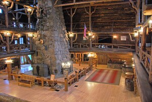 Interior rústico de una cabaña con chimenea de piedra, muebles de madera y una bandera.