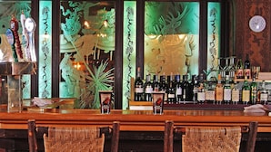 Un bar con sillas de mimbre, una variedad de botellas y cristalería decorativa.