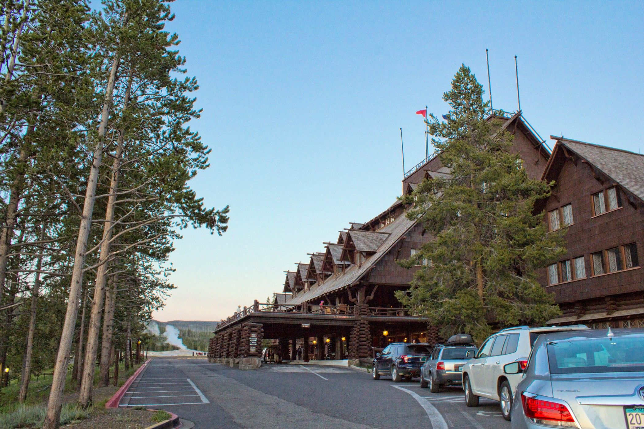A large log cabin-style building with a covered walkway, parked cars, and tall trees.