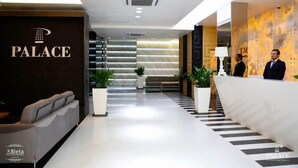Una moderna hall d'albergo con reception, area relax e una scala che conduce ai piani superiori.