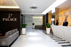 En modern hotellobby med en receptionsdisk, en sittgrupp och en trappa som leder upp till de övre våningarna.