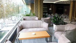 Un'area lounge moderna con un divano e un tavolo, vista attraverso ampie finestre, e una zona pranzo sullo sfondo.