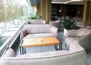 Ett modernt loungeområde med en soffa och ett bord, utsikt genom stora fönster och en matplats i bakgrunden.