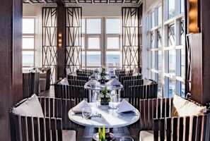 A dining area with a round table, multiple chairs, and a view of the sea. - Pullman Nadi Bay Resort and Spa Fiji (Nadi)