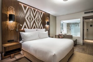 A modern hotel room with a large bed, two bedside tables, wall-mounted sconces, and a view of the bathroom. - Pullman Nadi Bay Resort and Spa Fiji (Nadi)