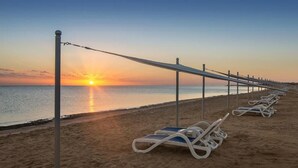Ein Strand mit Sonnenliegen, die entlang der Küste angeordnet sind, einer Geländer und dem Meer.