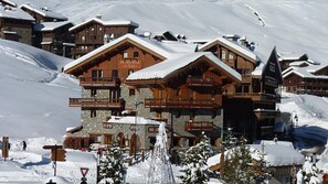 Un immeuble en bois à plusieurs étages, doté de balcons et d’une base en pierre, entouré de neige.