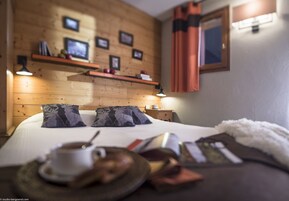A cozy bedroom with a wooden headboard, two pillows, a bedside table with a lamp, and a tray with a cup and saucer.