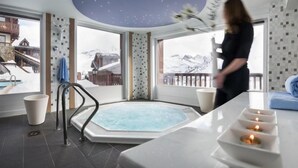 Ett spa-rum med ett bubbelbad, utsikt över snöklädda berg och en balkong med ett blått handduk.