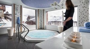 Une salle de spa avec un jacuzzi, une vue sur des montagnes enneigées et un balcon agrémenté d’une serviette bleue.
