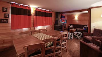 A wooden interior with a dining table, chairs, a sofa, and a television.