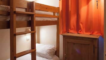 A bunk bed with a wooden headboard, a small wooden cabinet, and a curtain with a striped pattern.