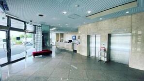 A modern lobby with a glass entrance, a reception desk, and elevators. - Reiah Hotel Kusatsu (Kusatsu)