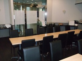 A conference room with a long table and chairs, a kitchen area with pots and pans, and a glass partition.