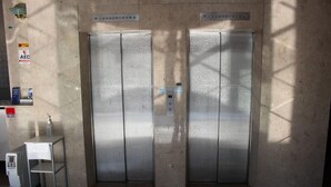An elevator with a control panel, a small table with a bottle, and an AED sign. - Reiah Hotel Kusatsu (Kusatsu)