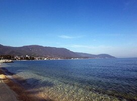 A coastal view with clear water, a beach, and a mountain in the background.