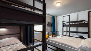 Quarto estilo dormitório com beliches, televisão de tela plana e janela com cortinas.