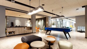 Um lobby moderno com mesa de pebolim, áreas de estar e balcão de recepção.