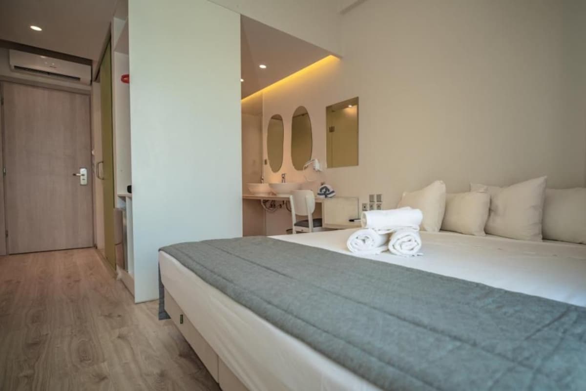 Ein Hotelzimmer mit einem großen Bett, einem Schreibtisch mit Stuhl, einem Spiegel und einer Tür.