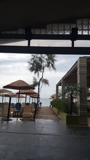 A covered outdoor seating area with umbrellas, a pathway leading to the beach, and a view of the sea. - Selyria Resort (Zakynthos)