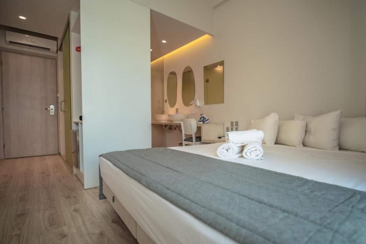 Una habitación de hotel con una cama grande, un escritorio con silla, un espejo y una puerta.