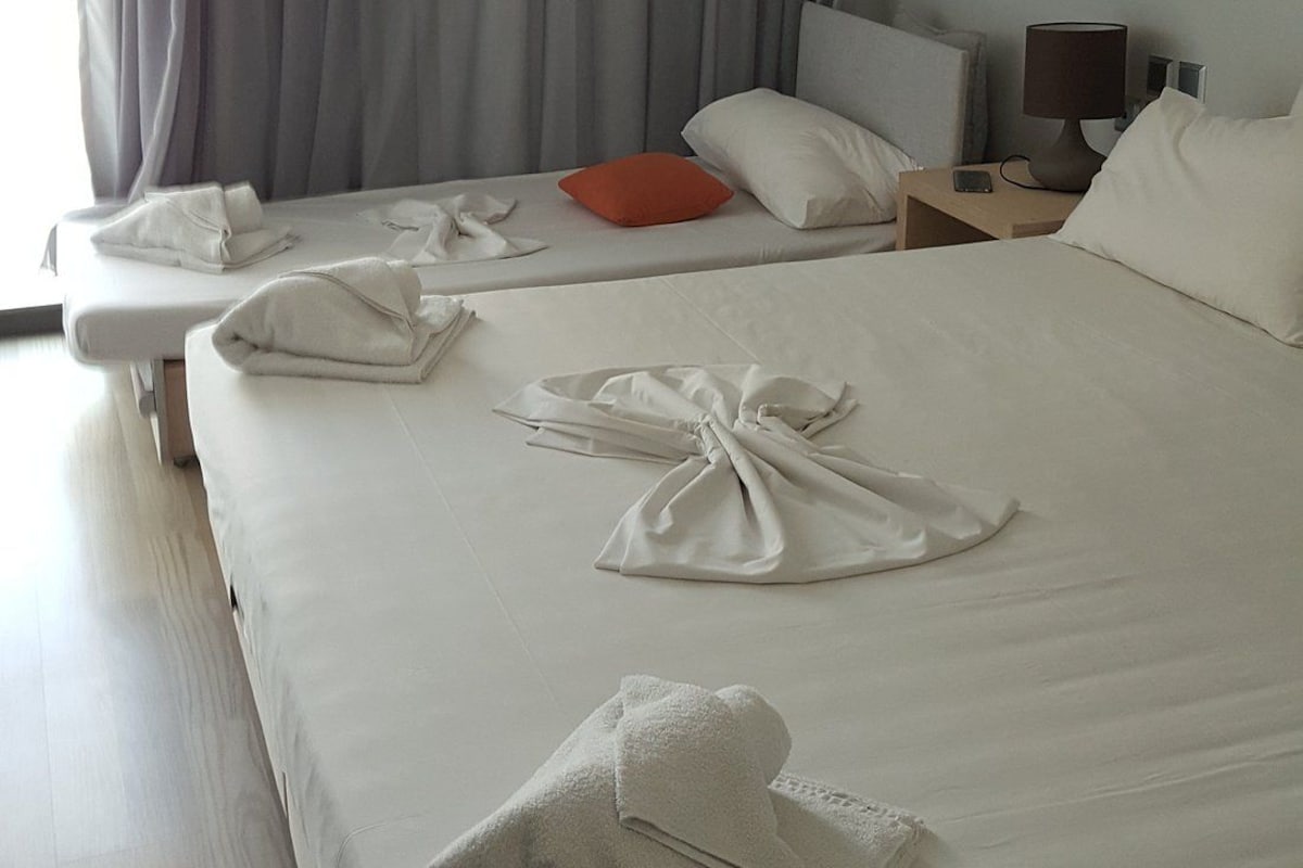 Ein Hotelzimmer mit einem großen Bett, zwei Nachttischen, einer Lampe und einem Fenster mit Vorhängen.