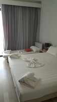 Una habitación de hotel con una cama grande, dos mesitas de noche, una lámpara y una ventana con cortinas.