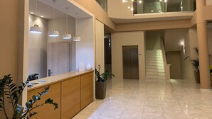 Um hall amplo com balcão de atendimento, escada e um lustre moderno.