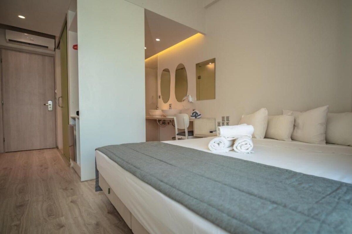 A hotel room with a large bed, a desk with a chair, a mirror, and a door.