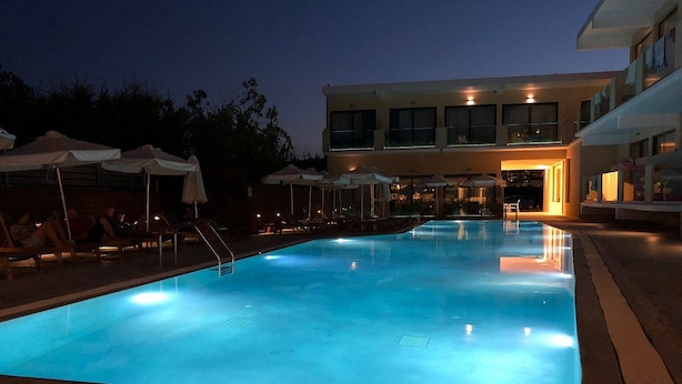 Piscina com espreguiçadeiras e guarda-sóis, rodeada por um edifício com vários andares e janelas.