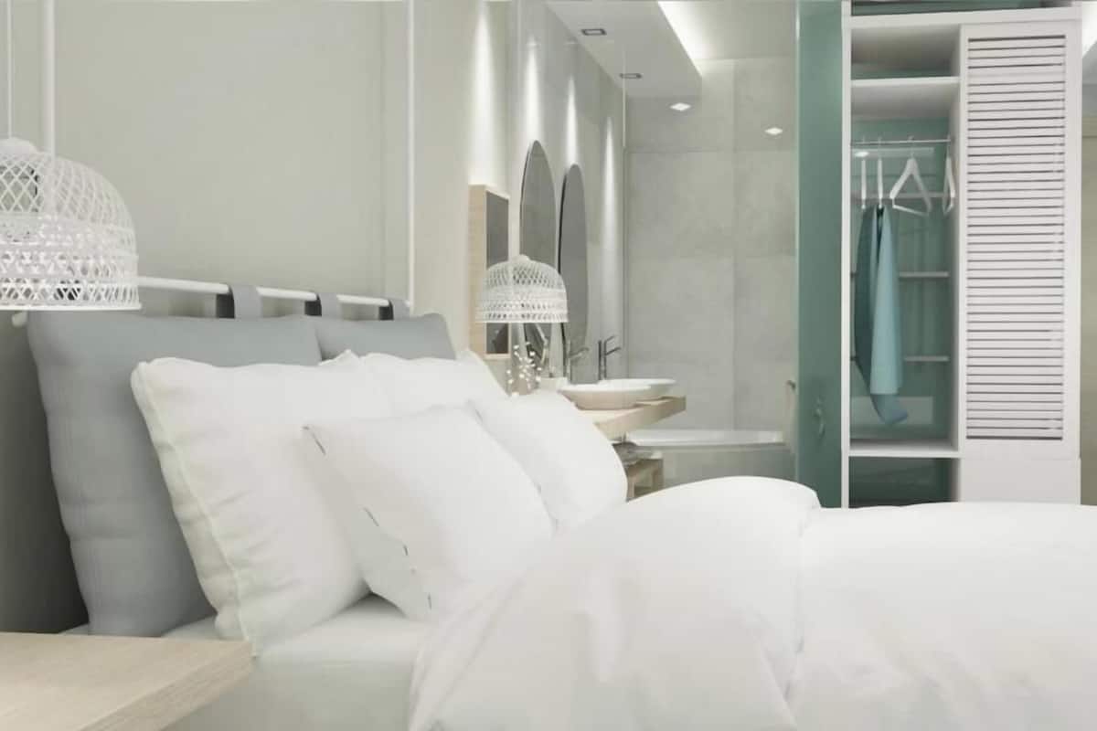 Un dormitorio moderno con cama, ropa de cama blanca, una mesita de noche, una lámpara colgante, un espejo y un vestidor.