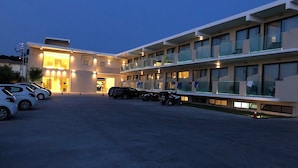 Um hotel moderno com estacionamento, vários andares e uma varanda com guarda-corros de vidro.