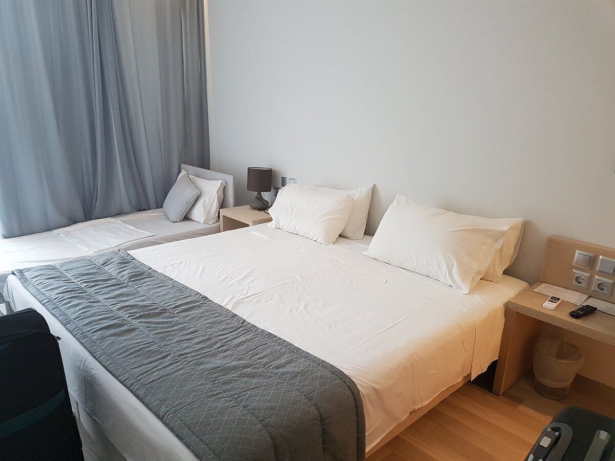 Una habitación de hotel con cama, mesitas de noche, escritorio, silla y ventana con cortinas.