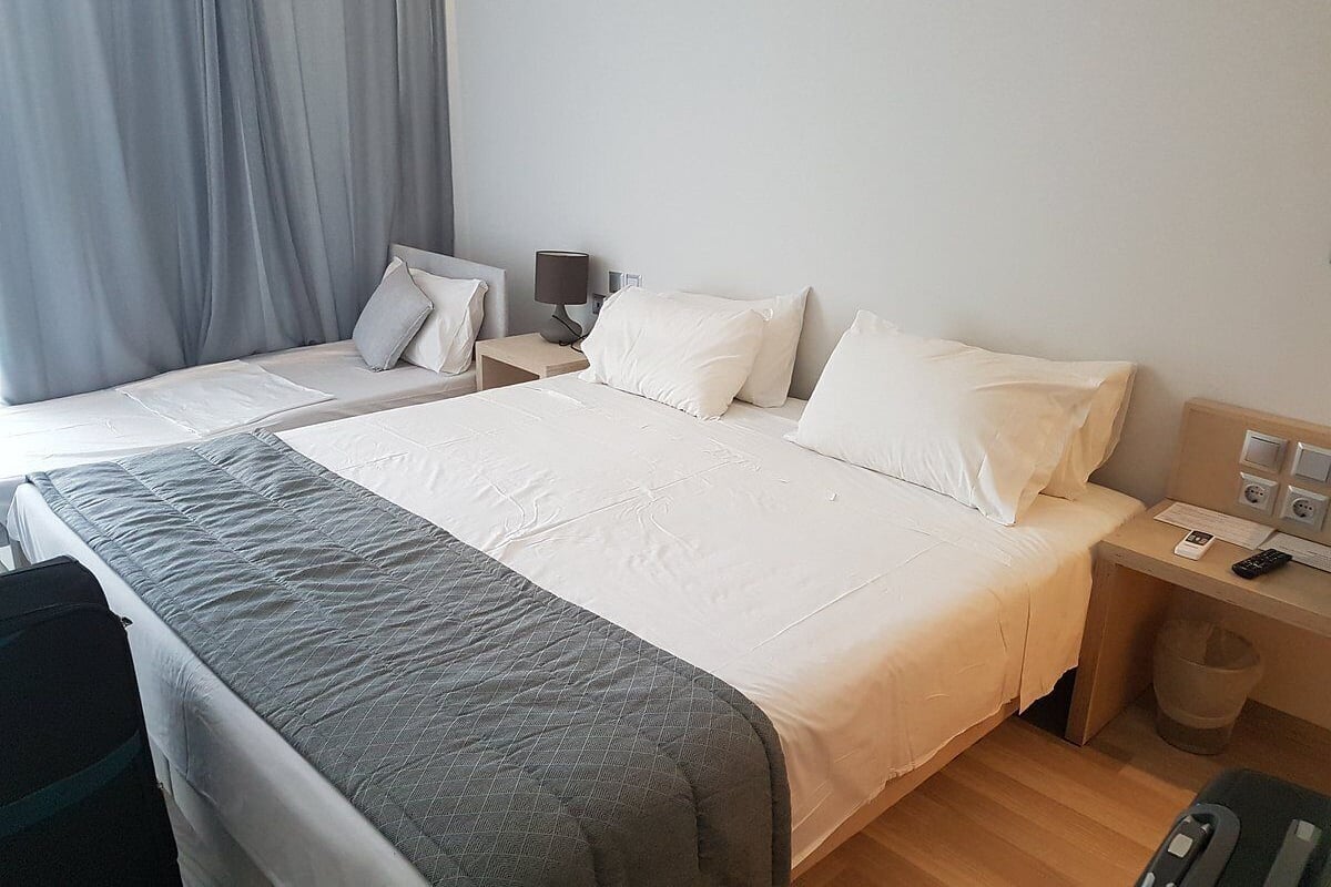 Una habitación de hotel con cama, mesitas de noche, escritorio, silla y ventana con cortinas.