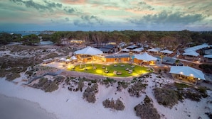Eine Vogelperspektive zeigt einen luxuriösen Resortkomplex mit mehreren überwasserbungalows, einem zentralen Gebäude und einer gepflegten Rasenfläche.