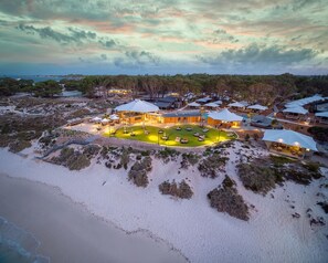 An aerial view of a resort with multiple overwater bungalows, a central building, and a well-maintained lawn area. - Discovery Holiday Parks - Rottnest Island (Perth)