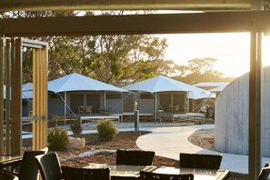 A series of tents with attached tables and chairs, set in a landscaped outdoor area with trees and a concrete structure in the background. - Discovery Holiday Parks - Rottnest Island (Perth)