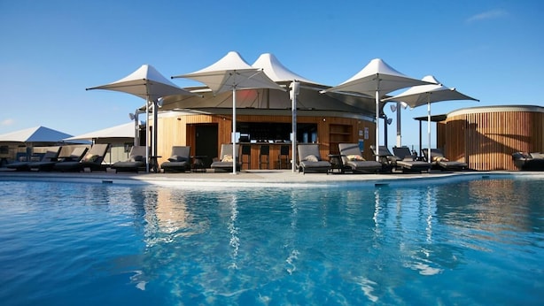 Ein Poolbereich mit Liegestühlen und Sonnenschirmen, eine Bar und ein Holzbau.