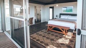 Un dormitorio con cama, ventilador de techo, ventana con vistas y puerta corrediza de vidrio que da a un área exterior.