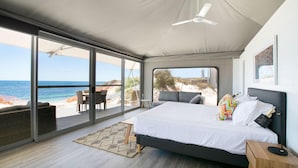 Ein Schlafzimmer mit Bett, Schreibtisch und Stuhl, mit Blick auf Strand und Meer.