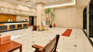 A hotel lobby with a reception desk, clocks, a potted plant, and a red carpet. - Shanghai Yuhang Hotel (Shanghai)