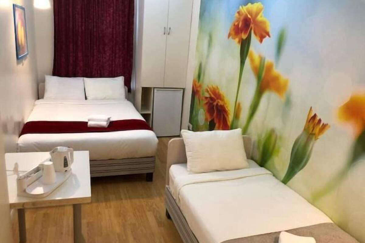 Ein Hotelzimmer mit zwei Betten, einem Schreibtisch mit Stuhl und einem Blumenbild an der Wand.