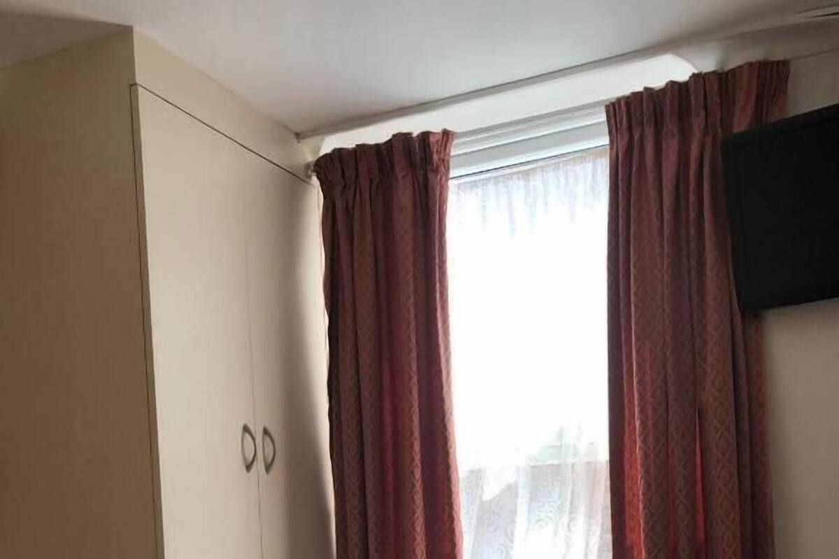 Ein Schlafzimmer mit Bett, Kleiderschrank und einem Fenster mit Vorhängen.