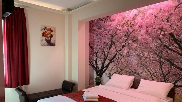 A hotel room with a large bed, a bedside table, a chair, and a wall with a cherry blossom mural. - Barking Hotel  (Barking)